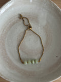 Gold bracelet with green beads on a white ceramic plate