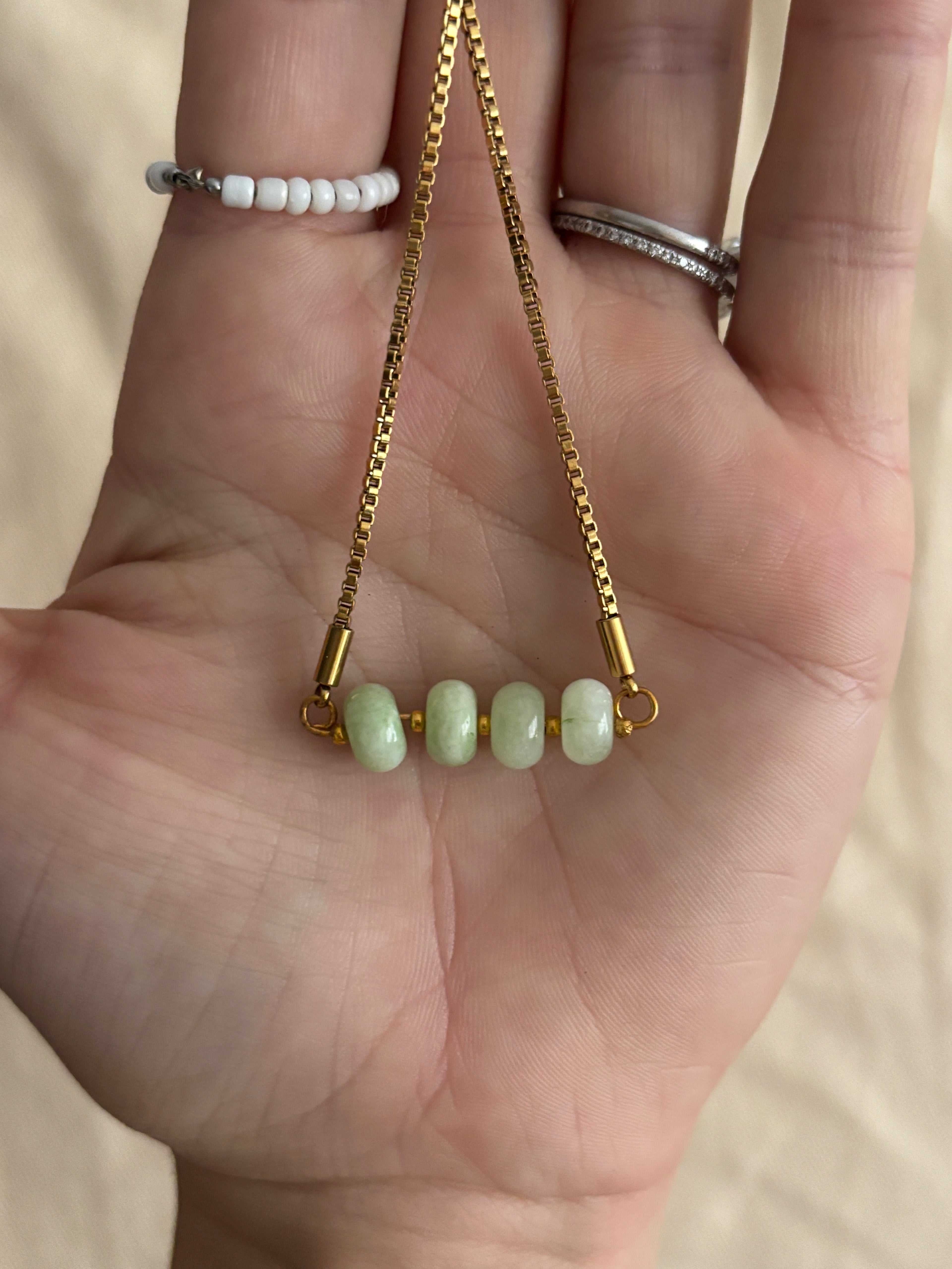 Gold chain with green beads held in a hand against a beige background