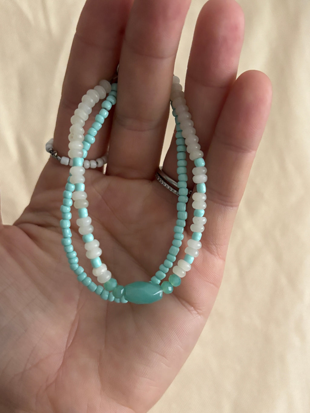 Hand holding two turquoise beaded bracelets on a beige background
