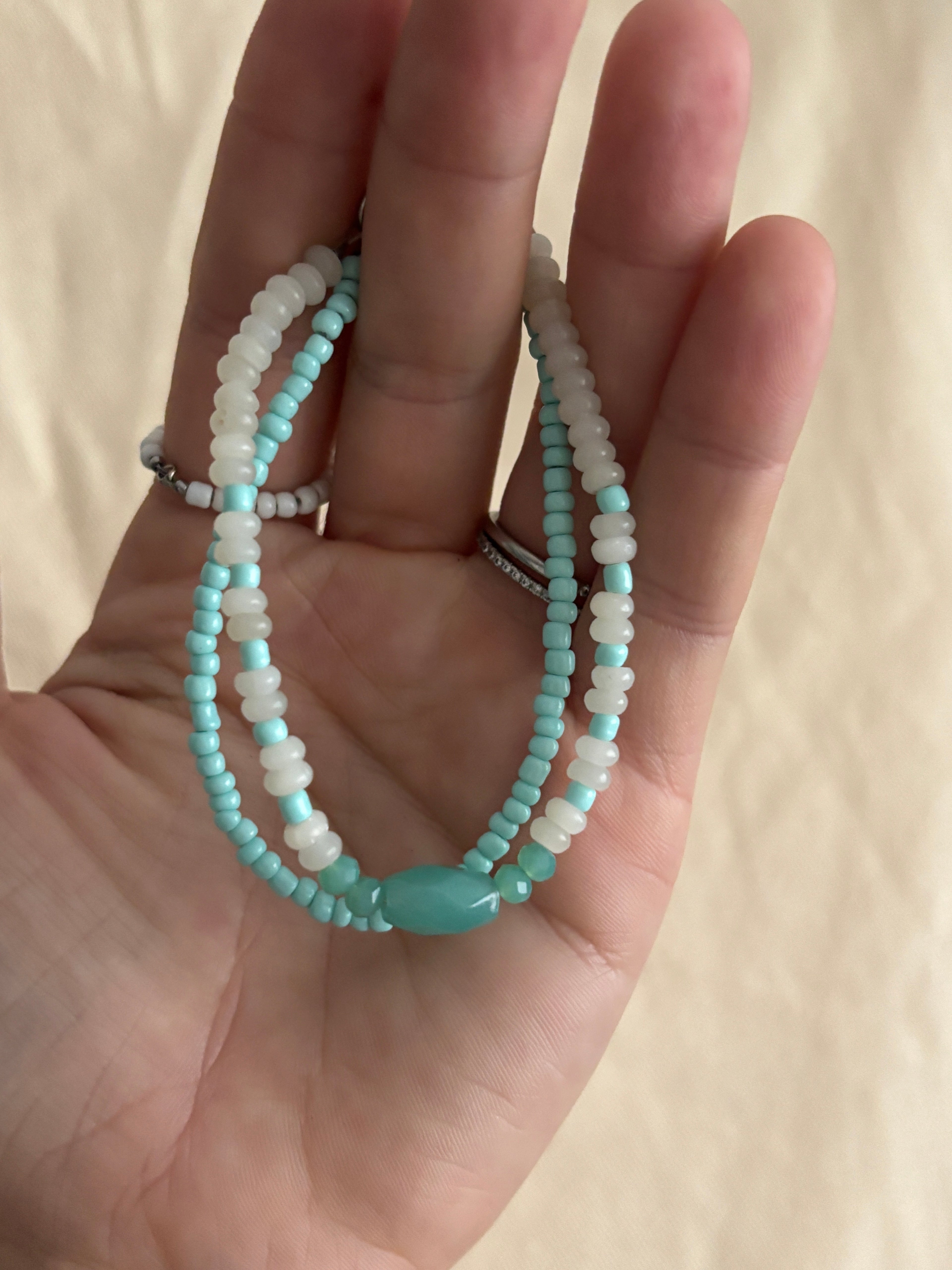Hand holding two turquoise beaded bracelets on a beige background