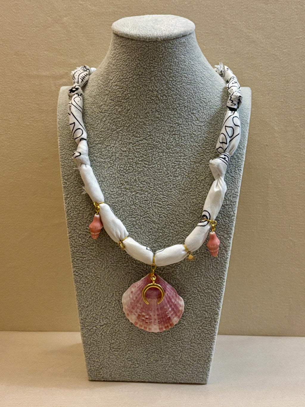 Necklace with shell pendant on a gray bust against a beige background