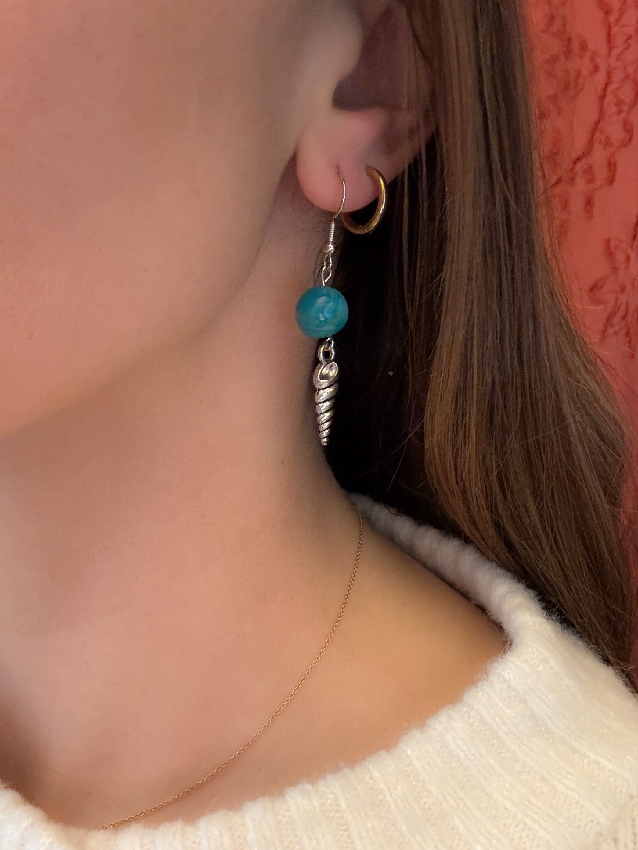 Close-up of an earring with a turquoise bead and silver chain on a person wearing a white sweater.