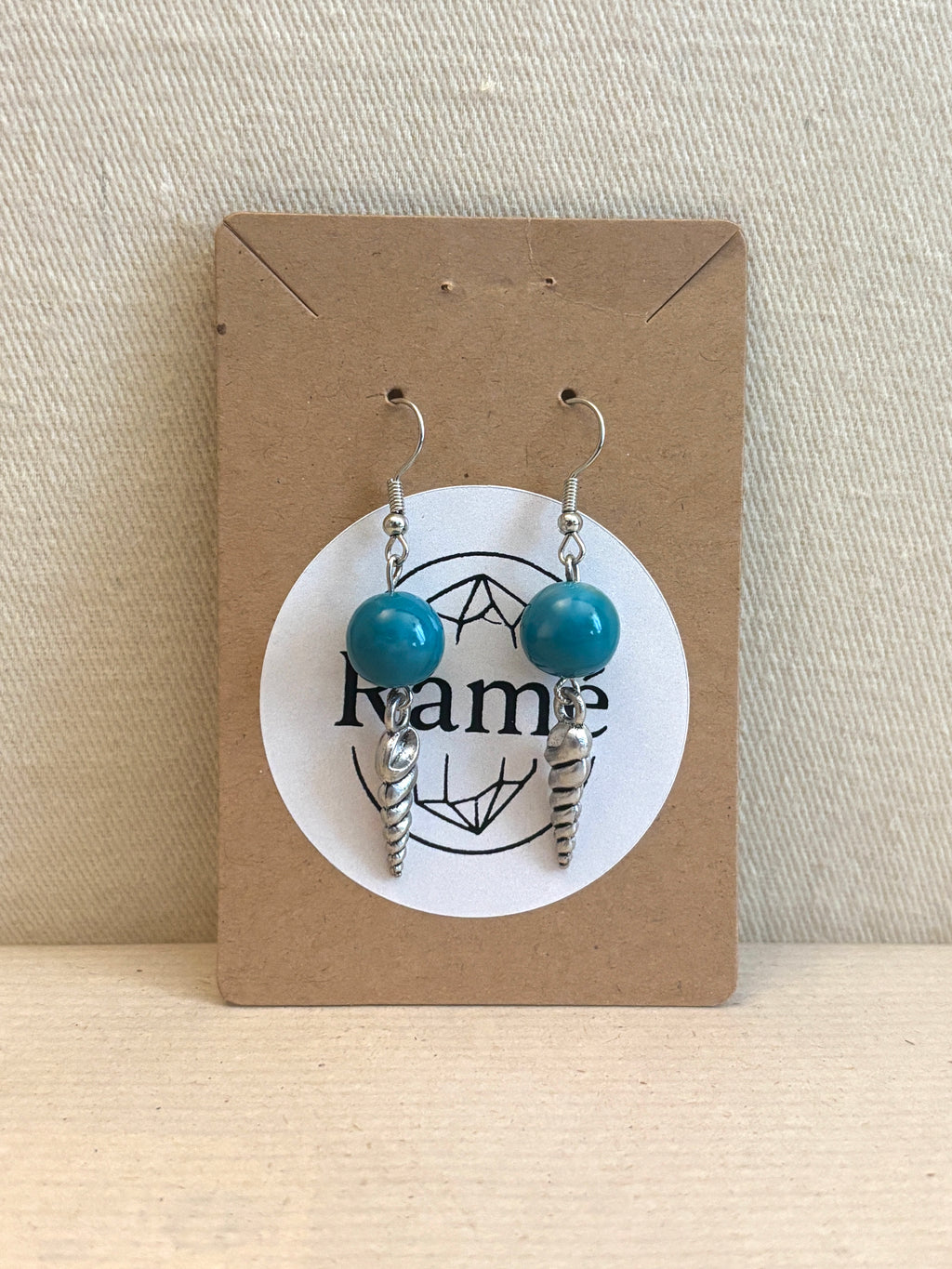 Pair of earrings with blue beads and silver accents on a Ramé branded card.