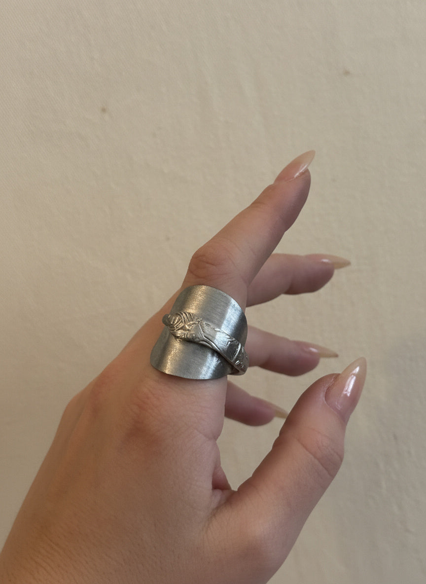 Hand wearing a silver ring against a plain background