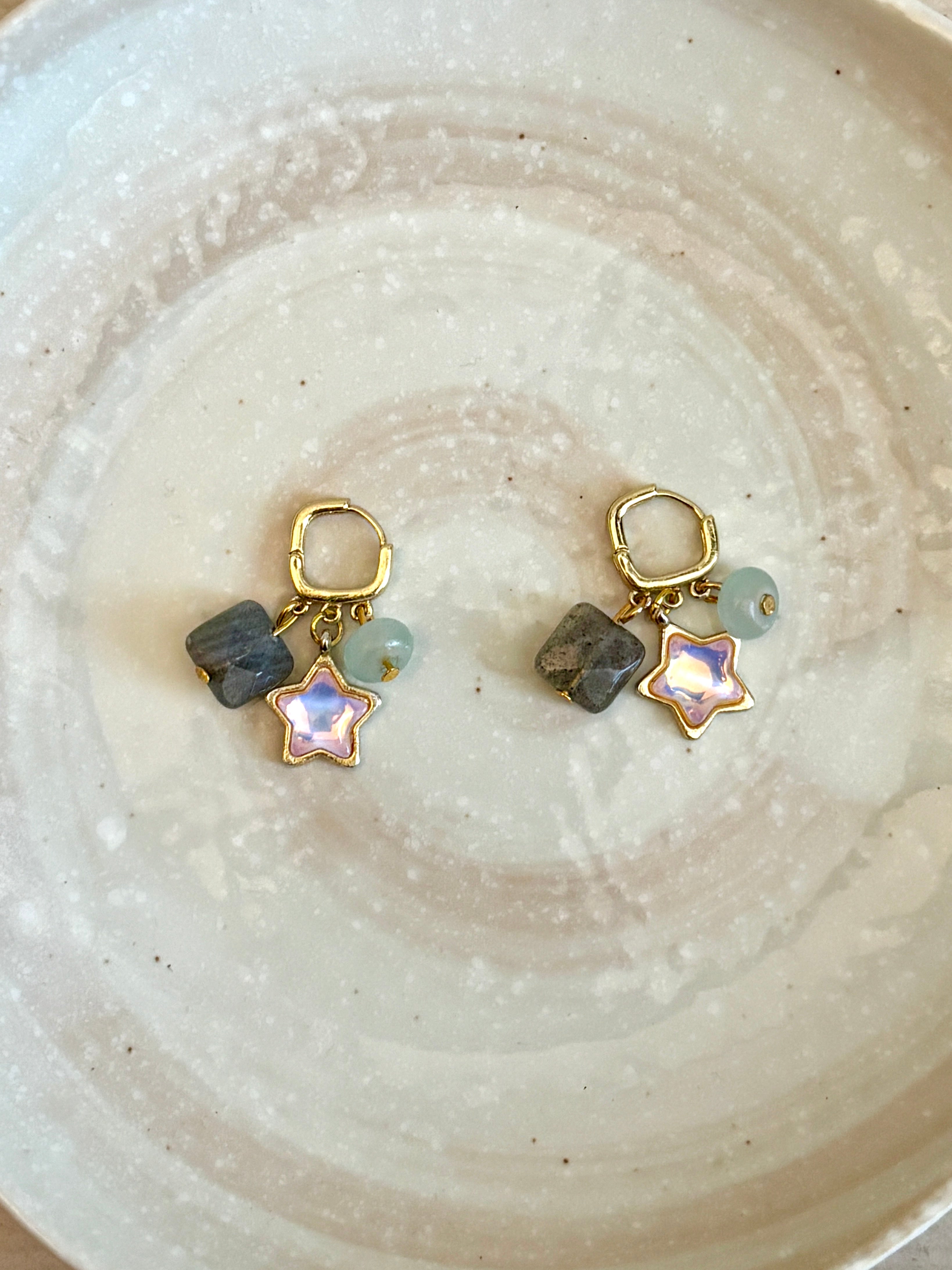 Pair of earrings with star-shaped charms and stones on a ceramic plate