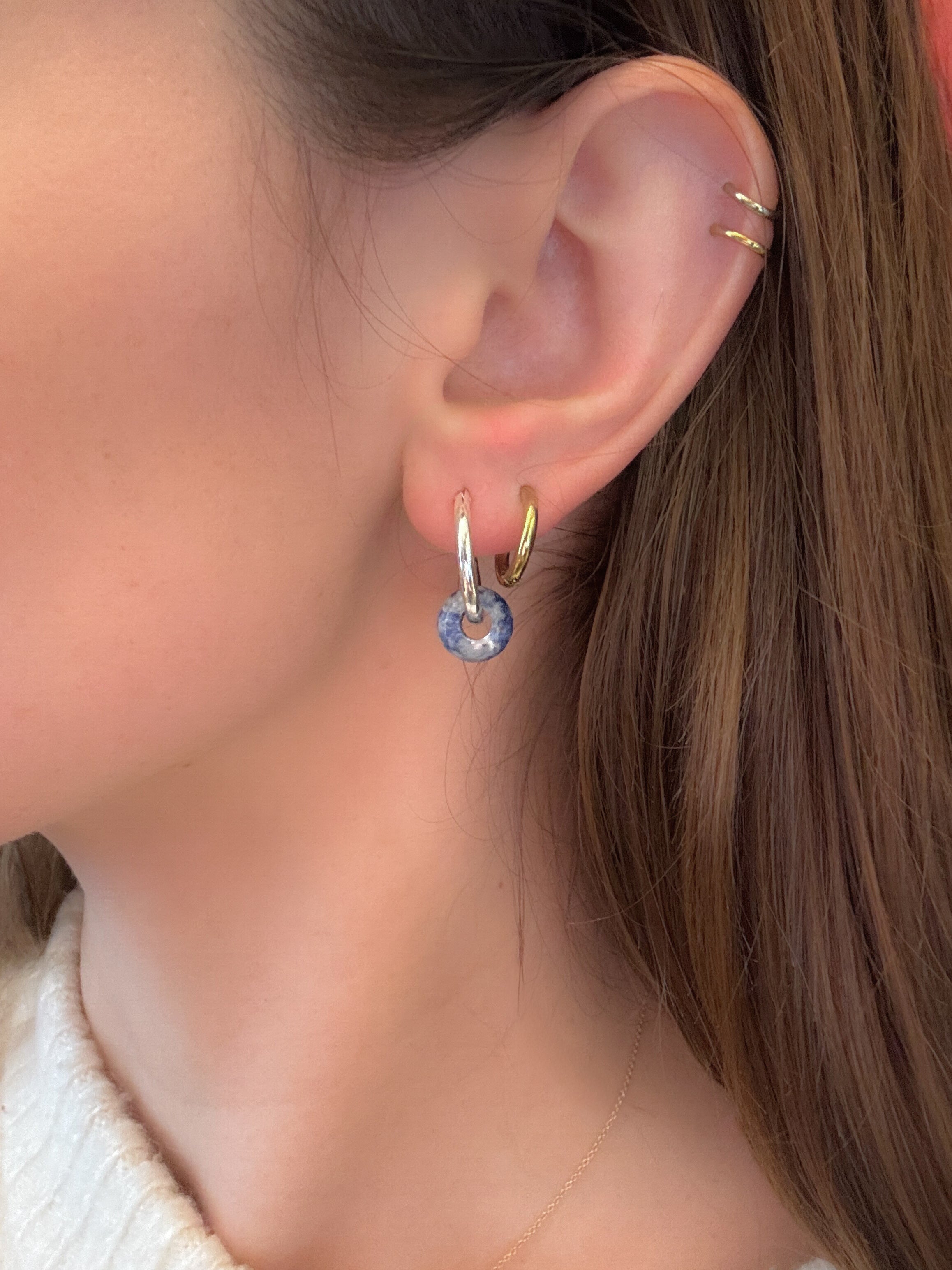 Close-up of an ear wearing gold hoop earrings with blue gemstones.