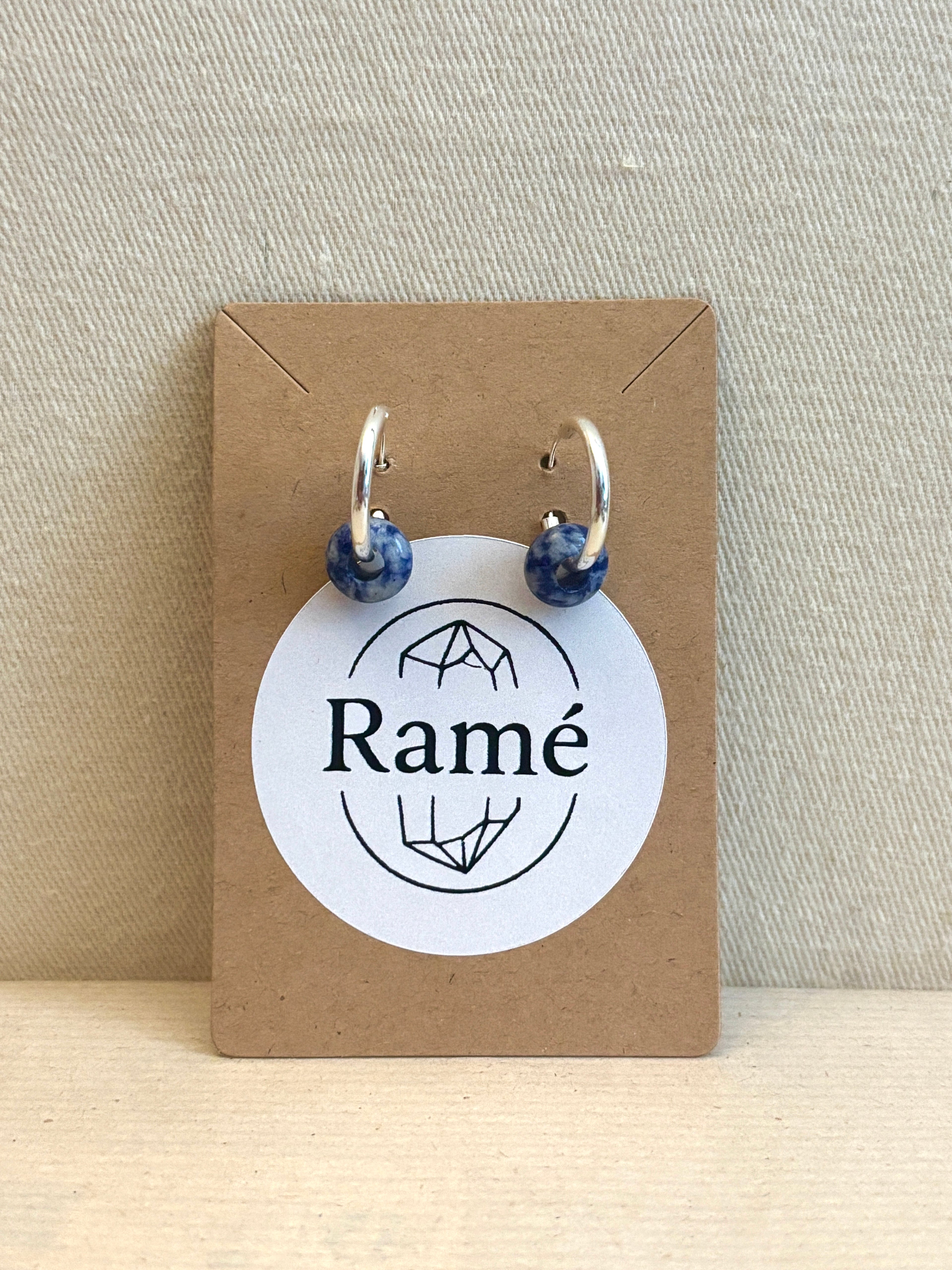 Pair of blue beaded earrings on a Ramé branded card against a beige background