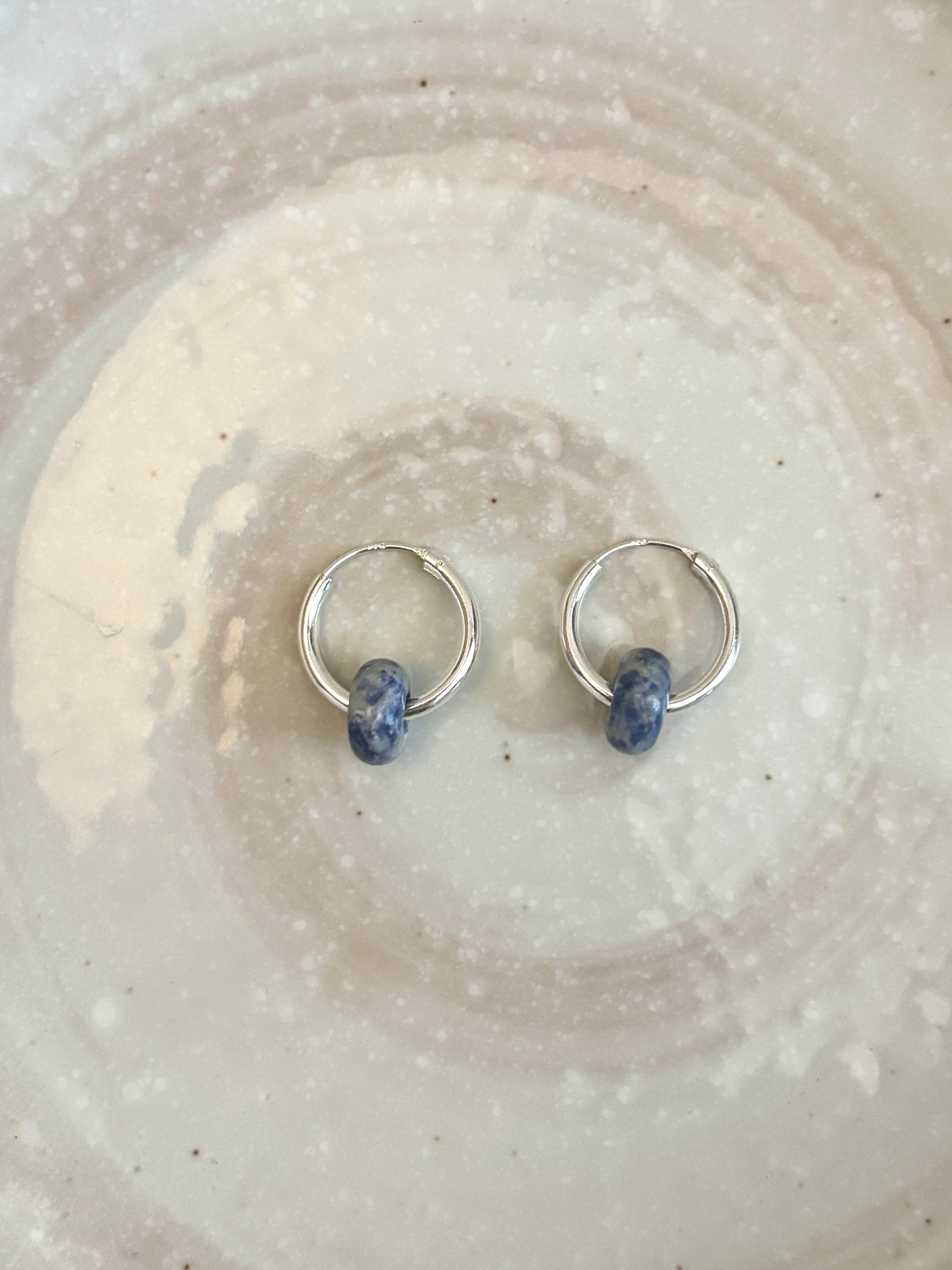 Silver hoop earrings with blue beads on a textured beige surface
