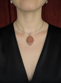 Person wearing a necklace with a pendant on a plain background