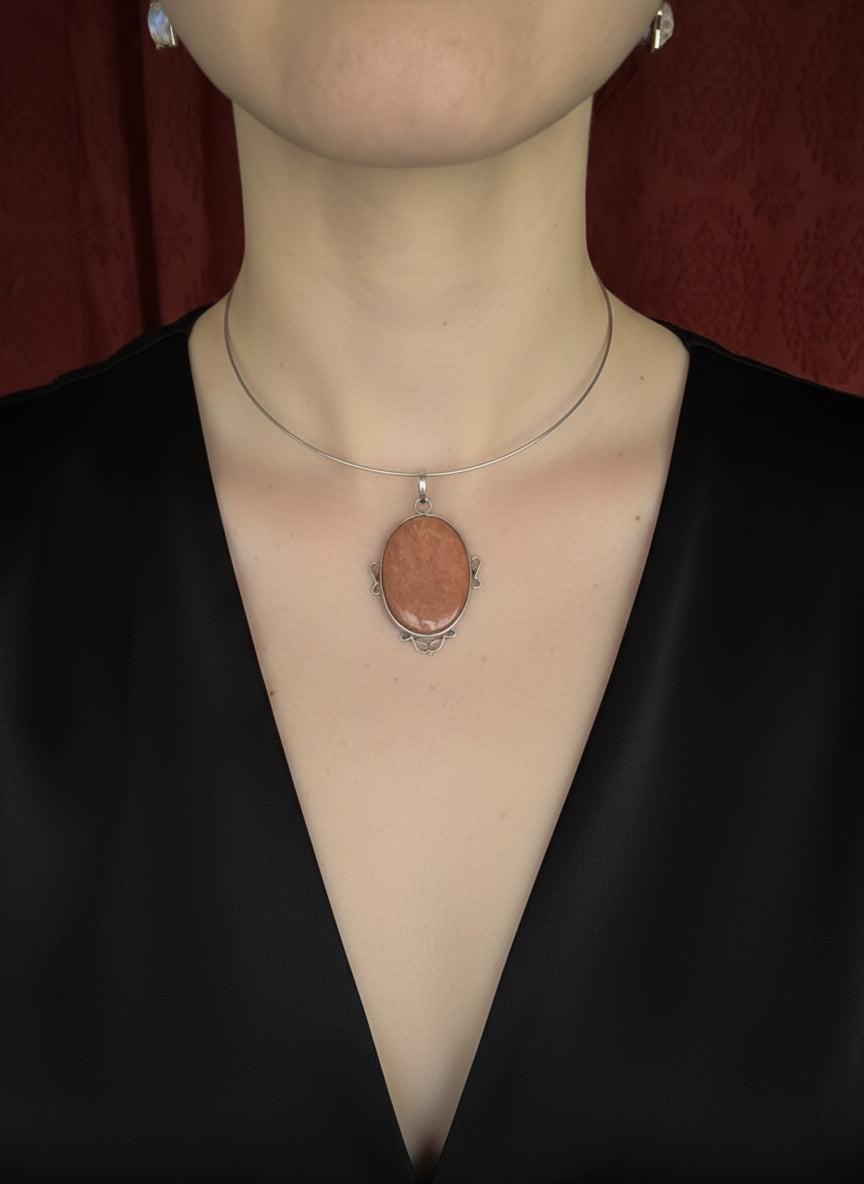 Person wearing a necklace with a pendant on a plain background
