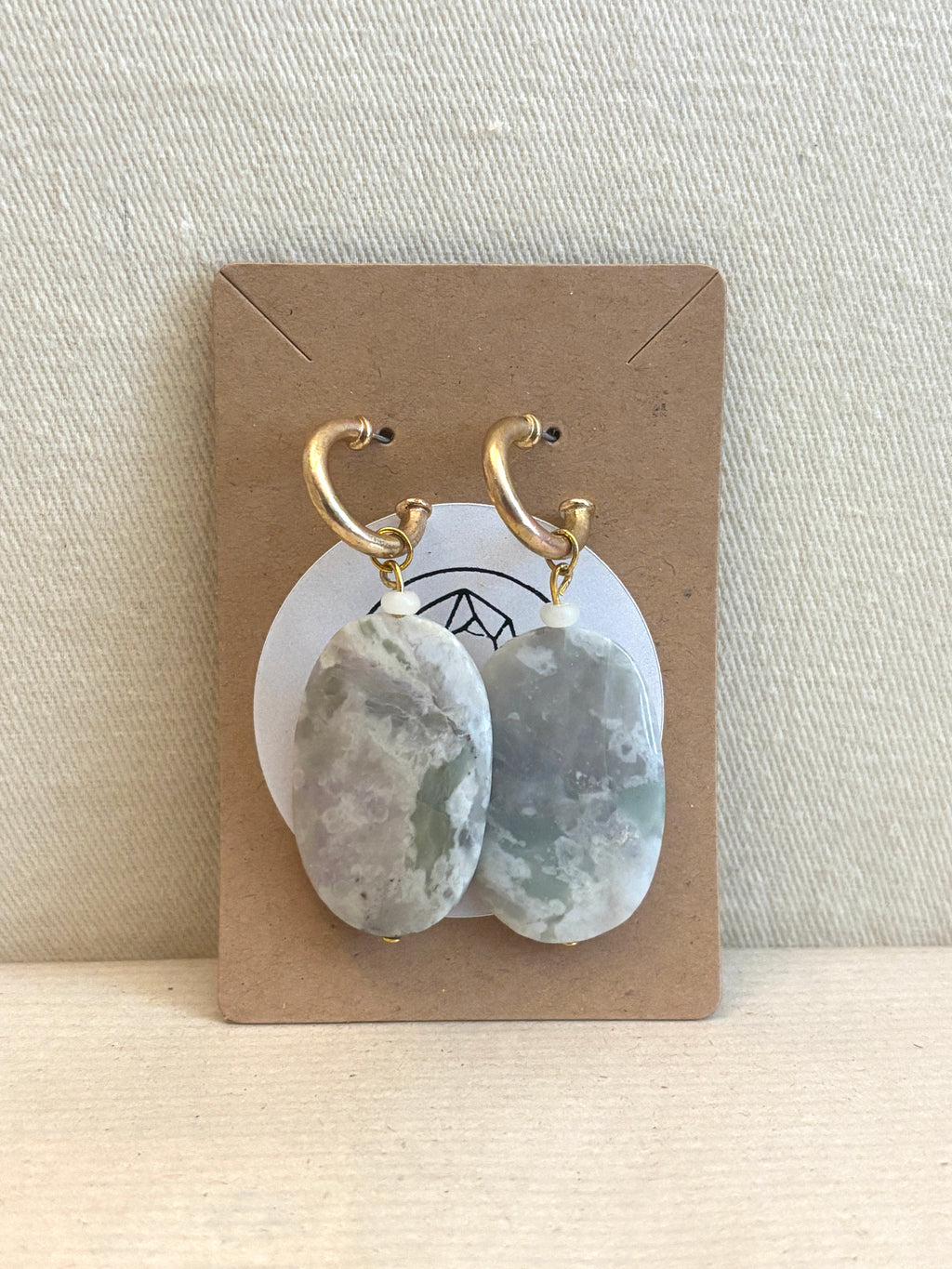 Pair of earrings on a display card with a beige background