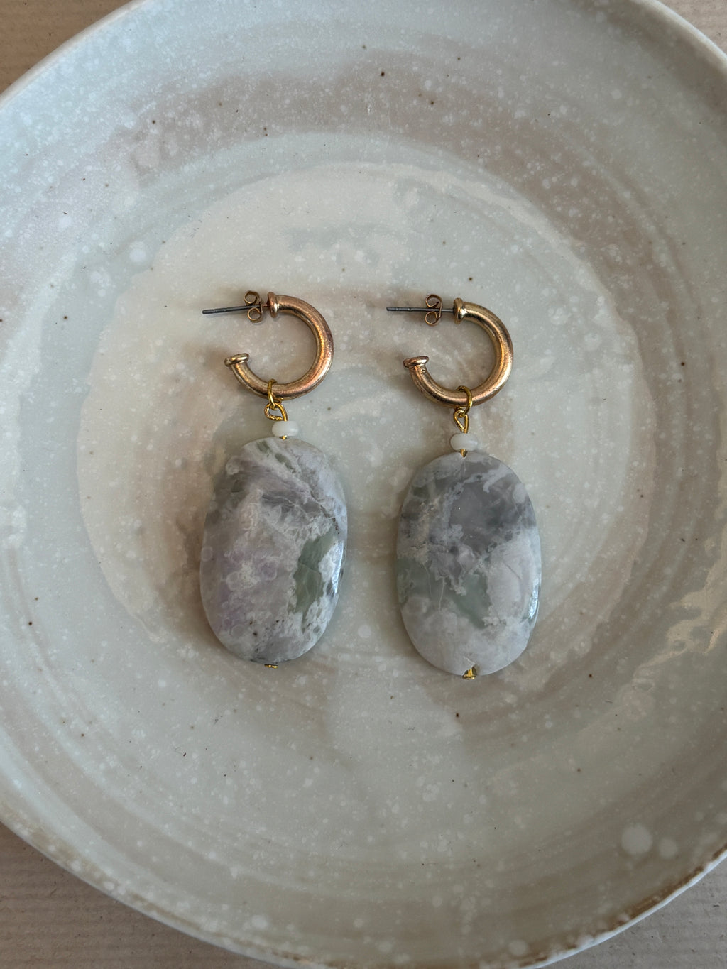 Pair of earrings with stone-like beads on a textured ceramic plate.