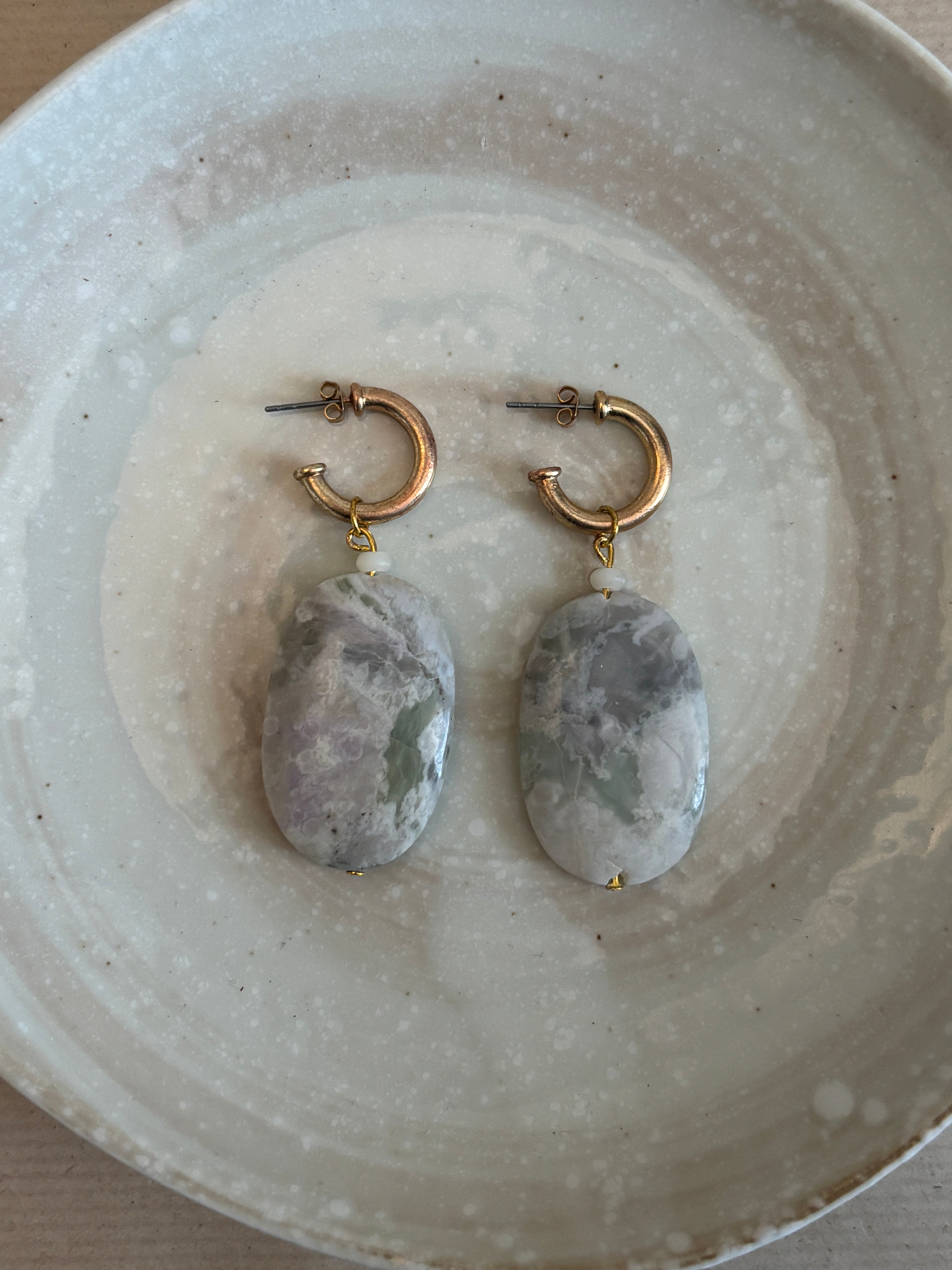 Pair of earrings with stone-like beads on a textured ceramic plate.