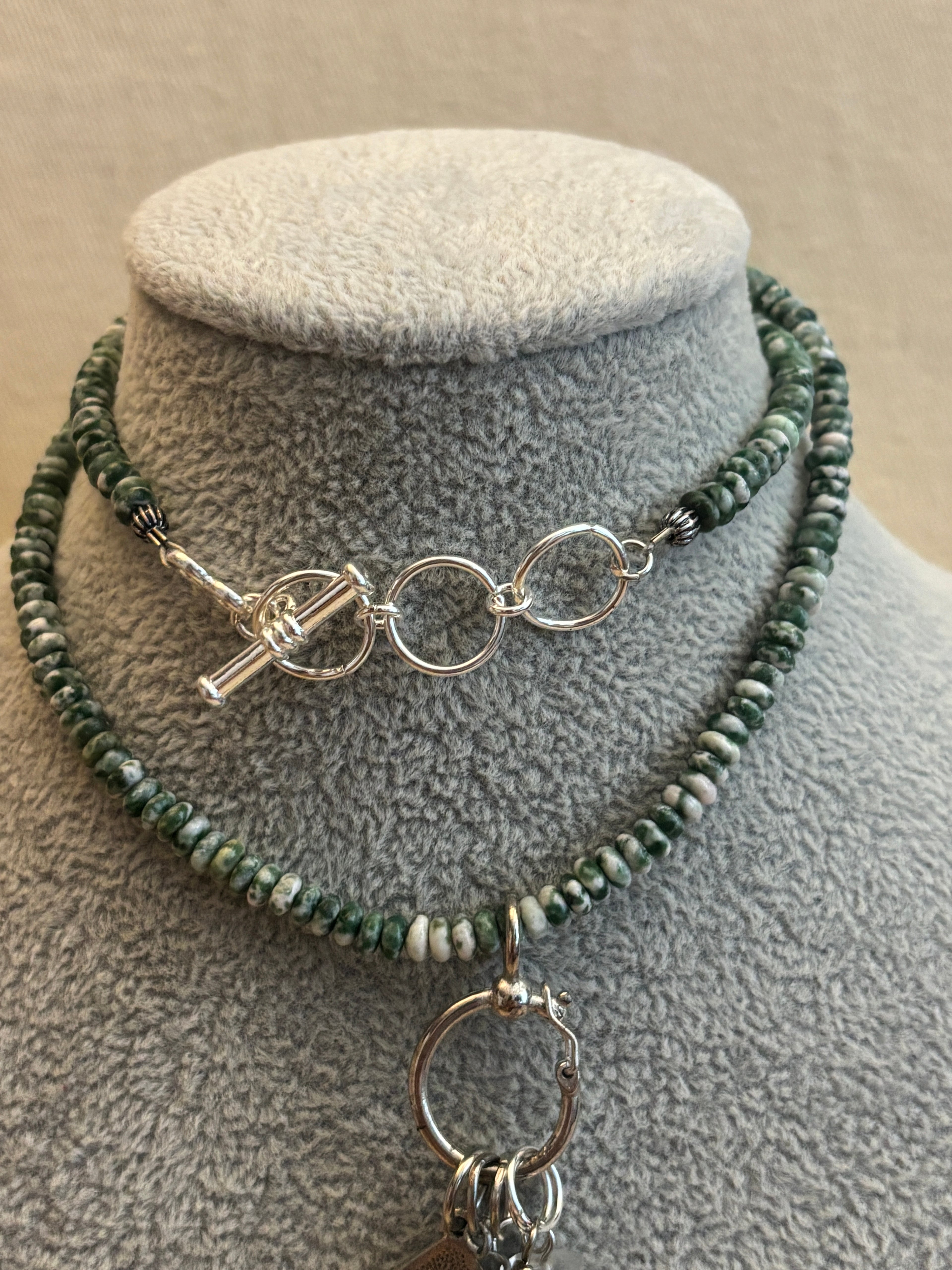 Necklace with green beads and silver clasp on a textured surface