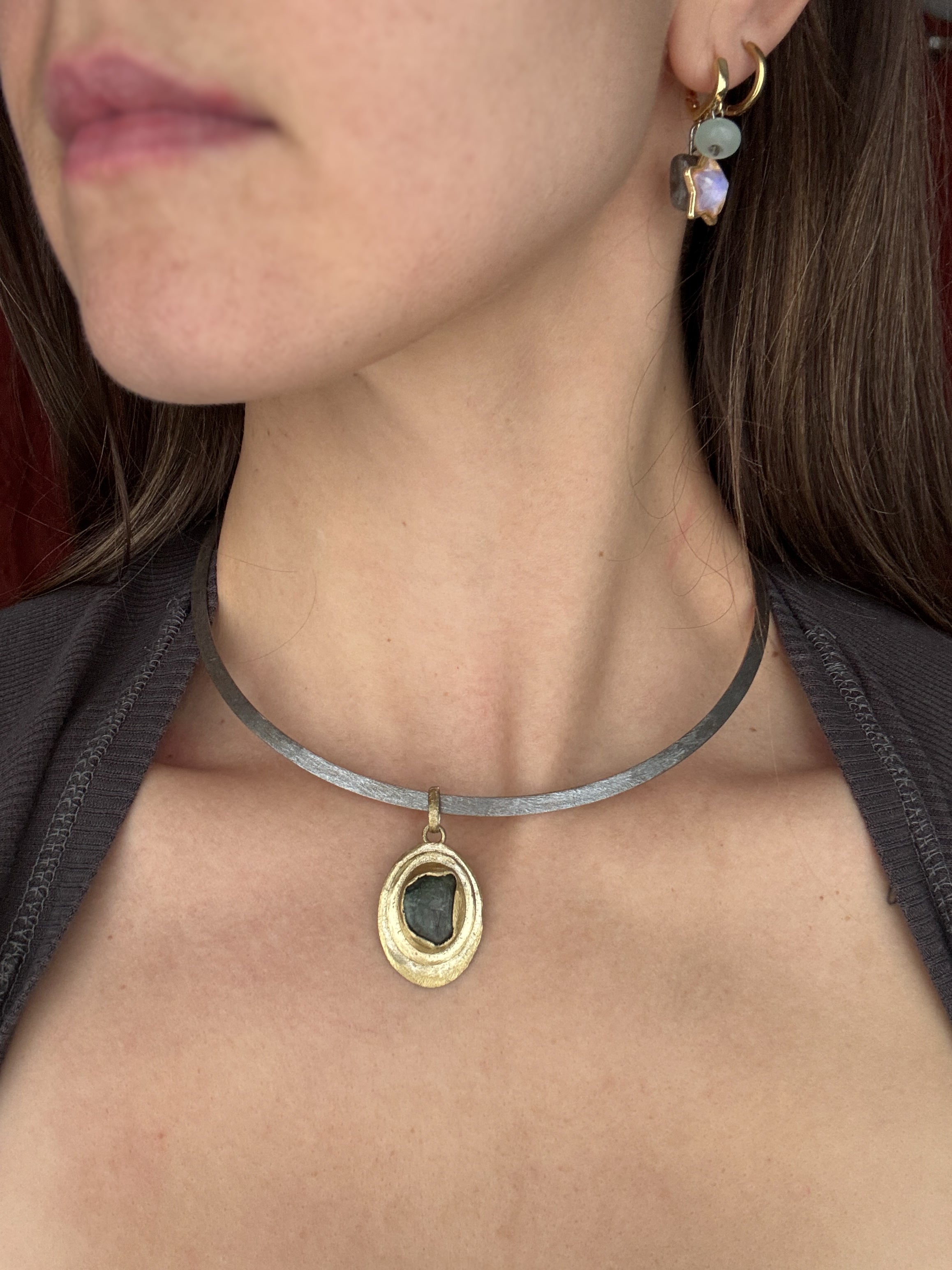 Close-up of a person wearing a gold necklace with a pendant and earrings.