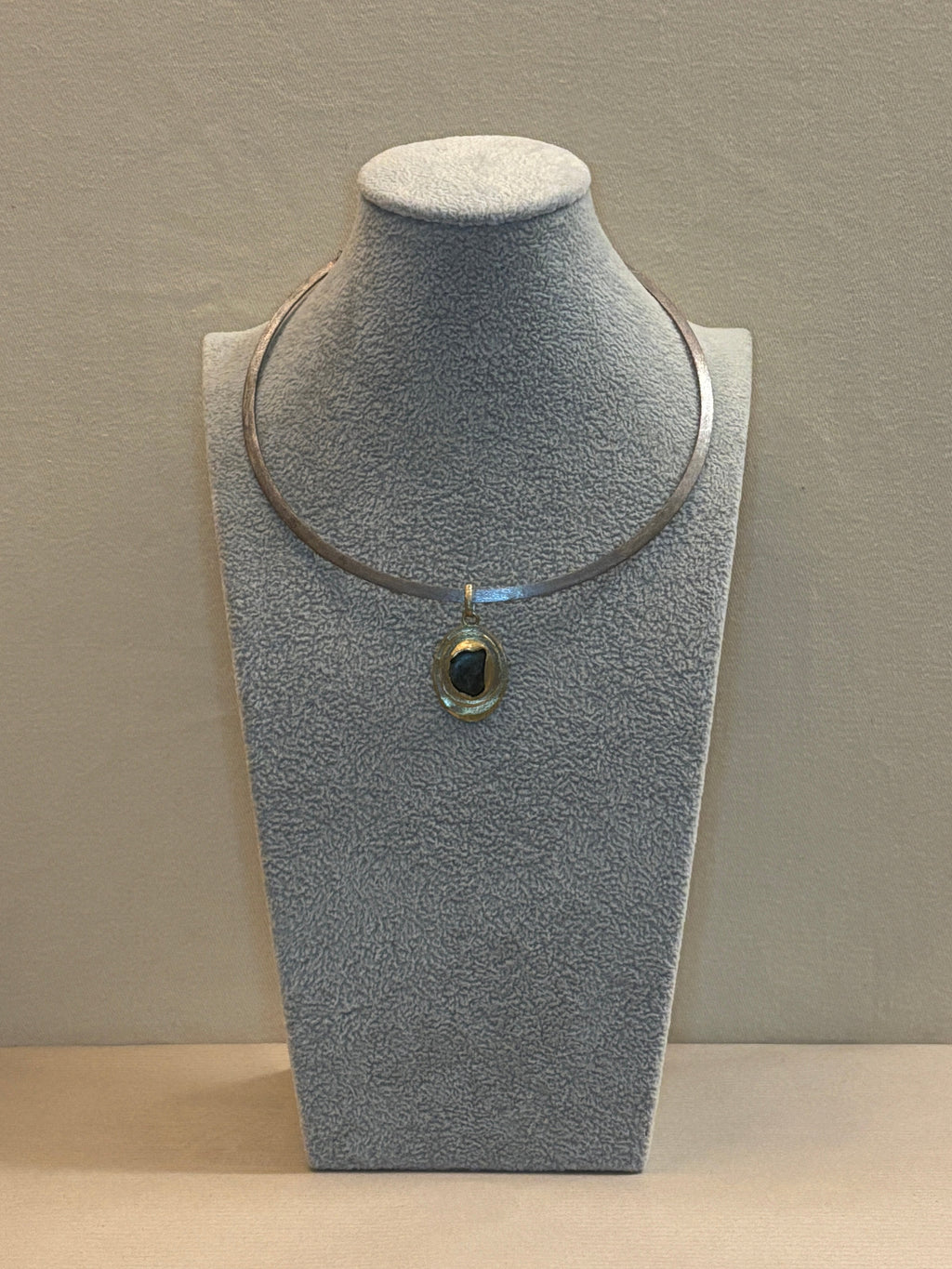Pendant necklace on a grey jewelry display.
