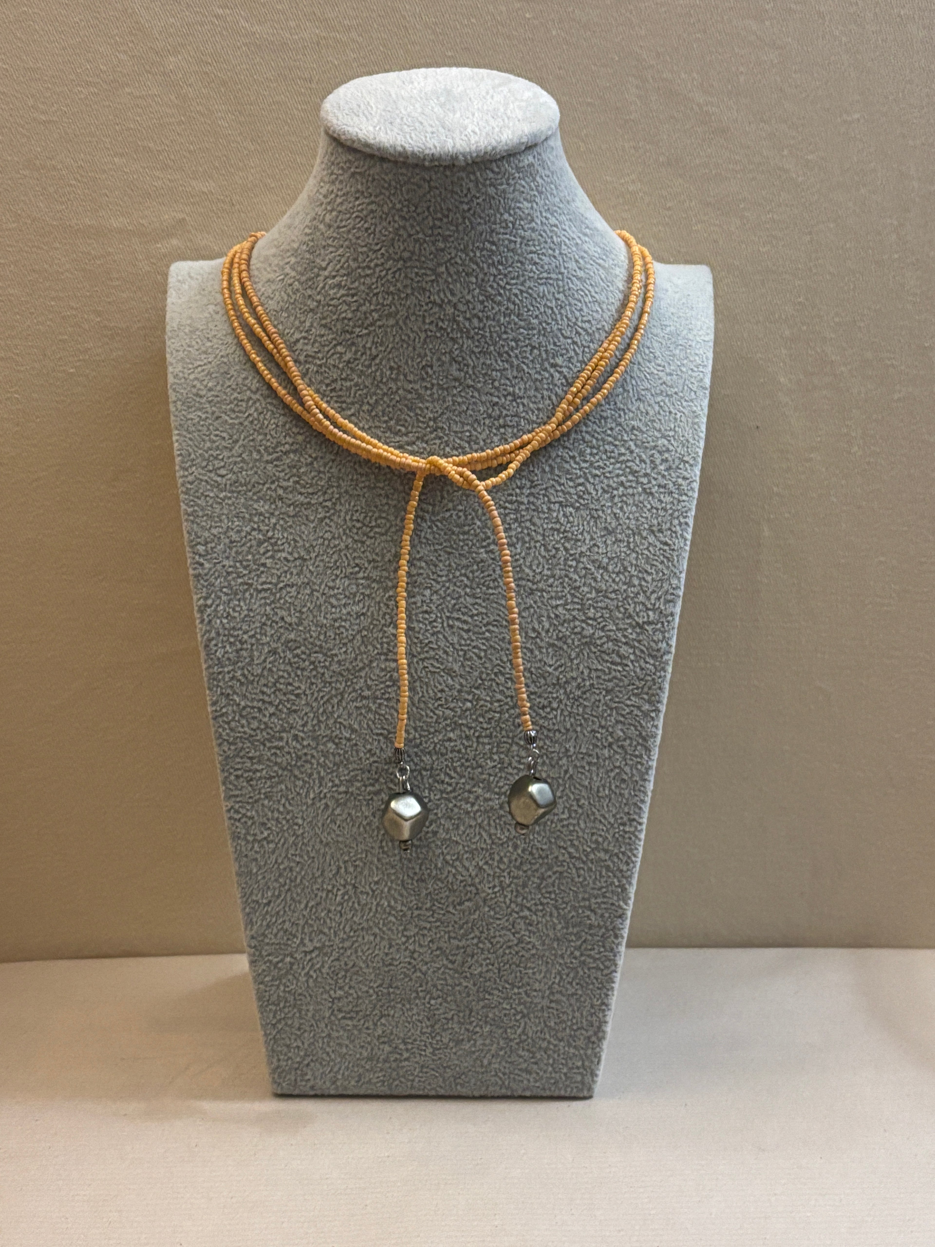 Jewelry display with beaded necklace on a gray mannequin bust against a beige wall.
