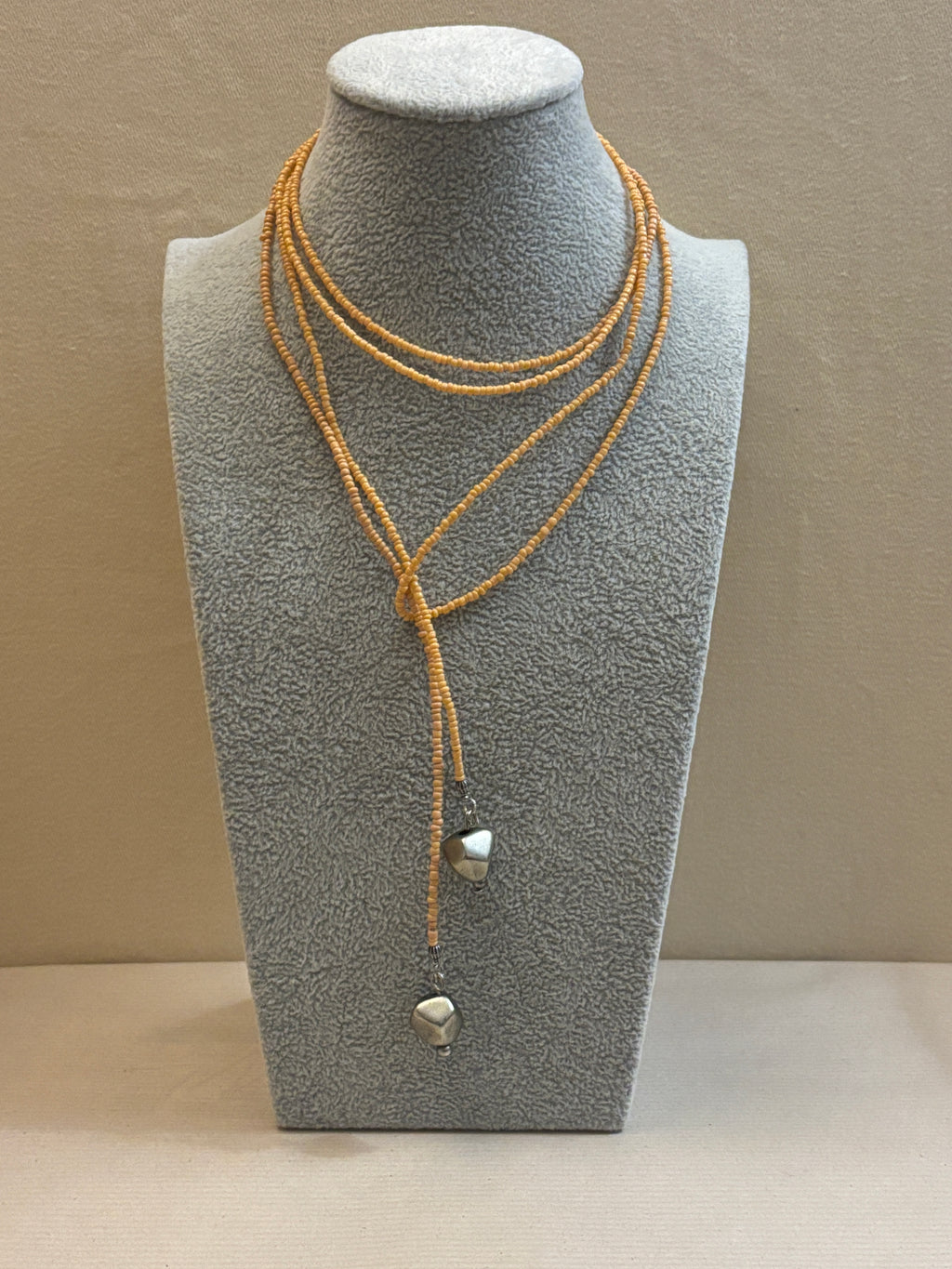 Gray jewelry display with beaded necklace on a neutral background