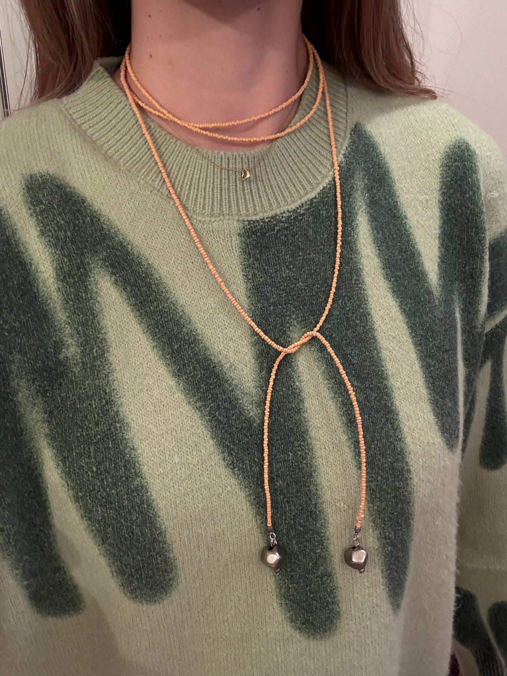 Close-up of a green sweater with a wrap around beaded necklace.